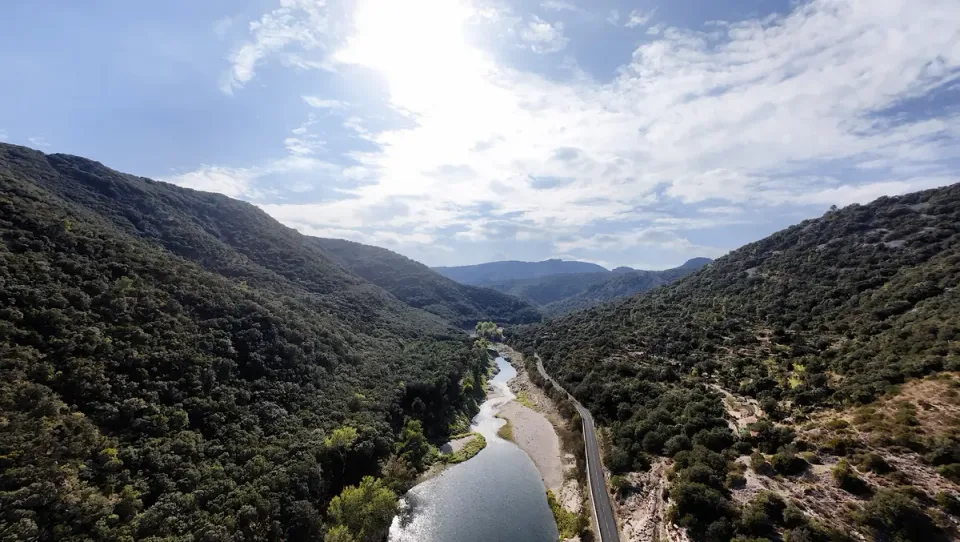 Reflected light on the Hérault River between wooded slopes with successive hills on the horizon and a road on the right