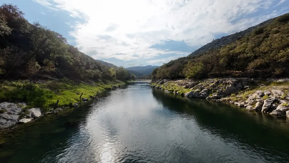Bright sky reflections on the Hérault River between rocky wooded banks, viewed close to the water