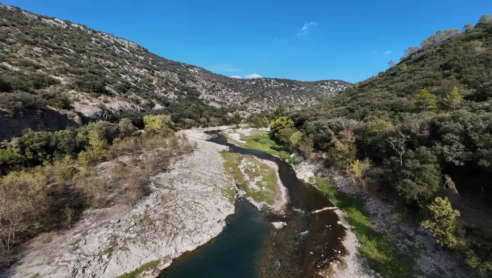 Pale exposed rock following the Hérault River with trees along the banks and hills beyond