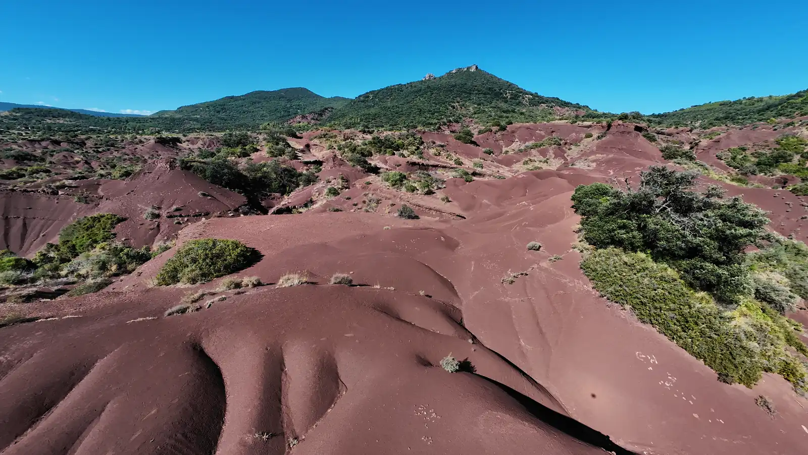 Rounded red ridges and shadowed gullies beneath a green hill at Canyon du Diable in southern France