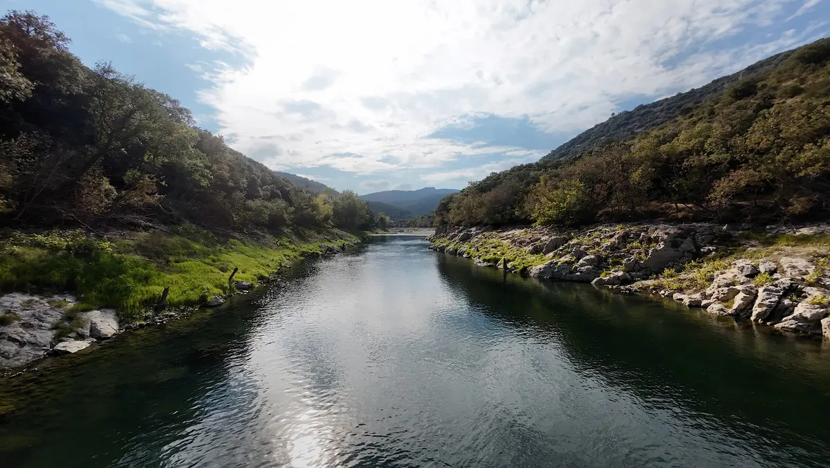 Bright sky reflections on the Hérault River between rocky wooded banks, viewed close to the water