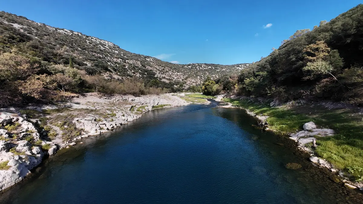 Dark blue water between a pale rocky bank on the left and a wooded slope on the right beneath a blue sky