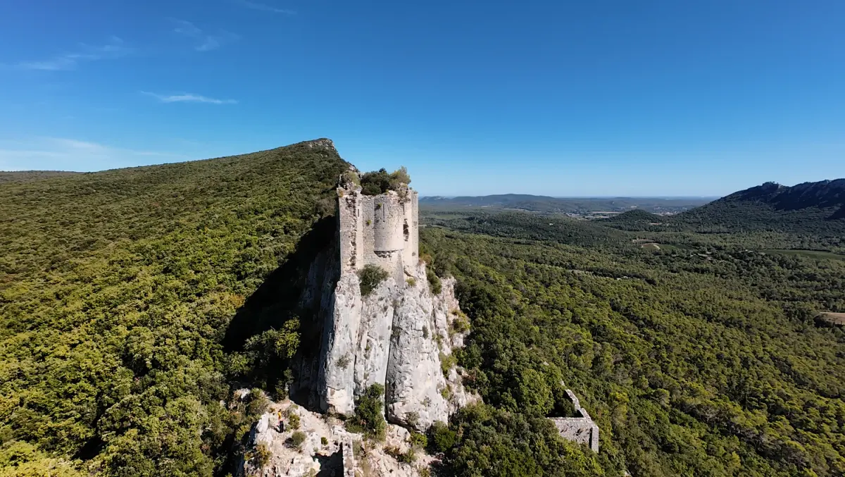 Pale walls of Viviourès Castle rising from a limestone outcrop above woodland